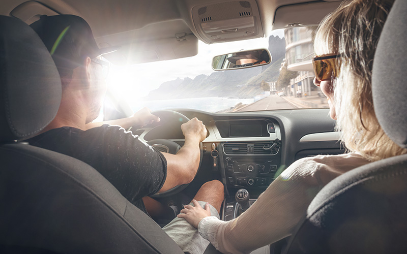 Coppia che guida un’auto a noleggio lungo la costa italiana, mostrando perché conviene noleggiare un’auto in Italia per la libertà di movimento e i panorami