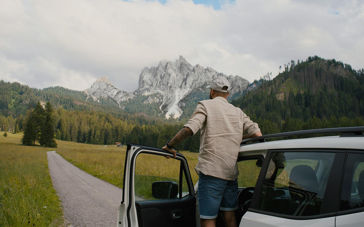 Viaggiatore fermo accanto a un’auto a noleggio tra le montagne italiane, a sottolineare quando noleggiare un’auto in Italia ha senso