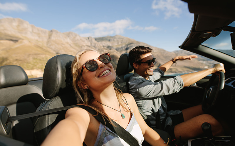 Bella donna in viaggio on the road con il suo ragazzo. Giovane coppia che si gode un viaggio in auto a bordo di una decappottabile.