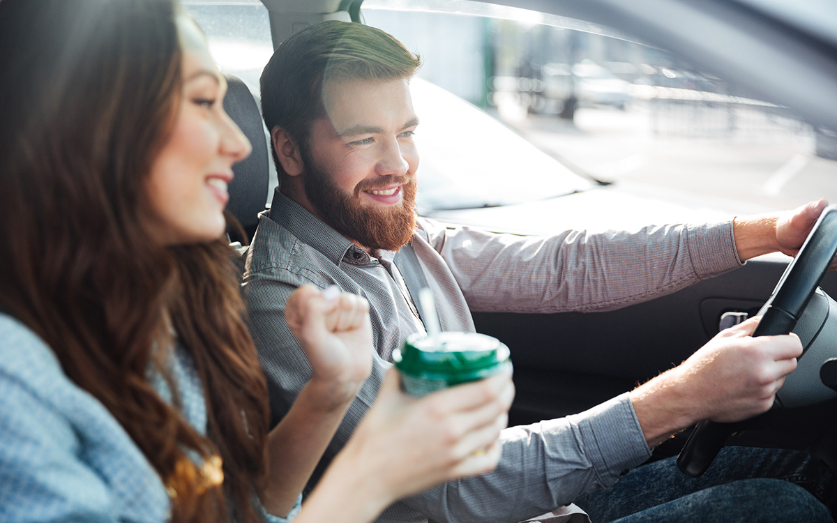 Bočni prikaz nasmiješenog para u automobilu, izrezana fotografija; muškarac za upravljačem.