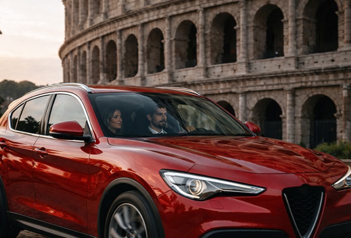 Red rental SUV driving past the Colosseum in Rome, showing how renting a car in Italy can be expensive in major tourist cities.