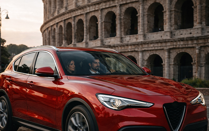 Rotes Mietwagen-SUV, das am Kolosseum in Rom vorbeifährt und zeigt, warum das Mieten eines Autos in großen italienischen Touristenstädten teuer sein kann.
