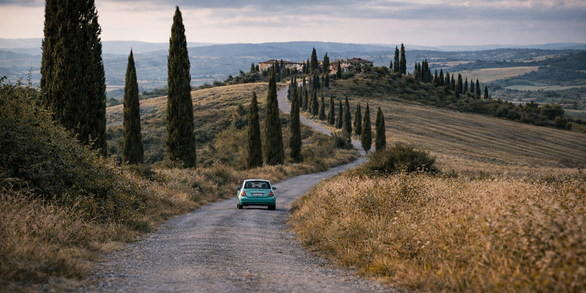 Small rental car driving through the Tuscan countryside, illustrating whether renting a car in Italy is expensive for rural travel.