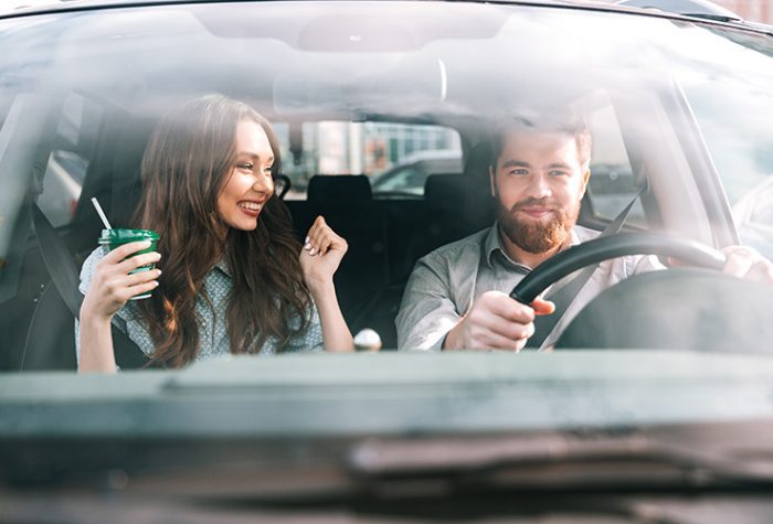 Young couple enjoying their drive after renting a car at Milan Bergamo Airport, smiling inside a modern rental vehicle on departure.