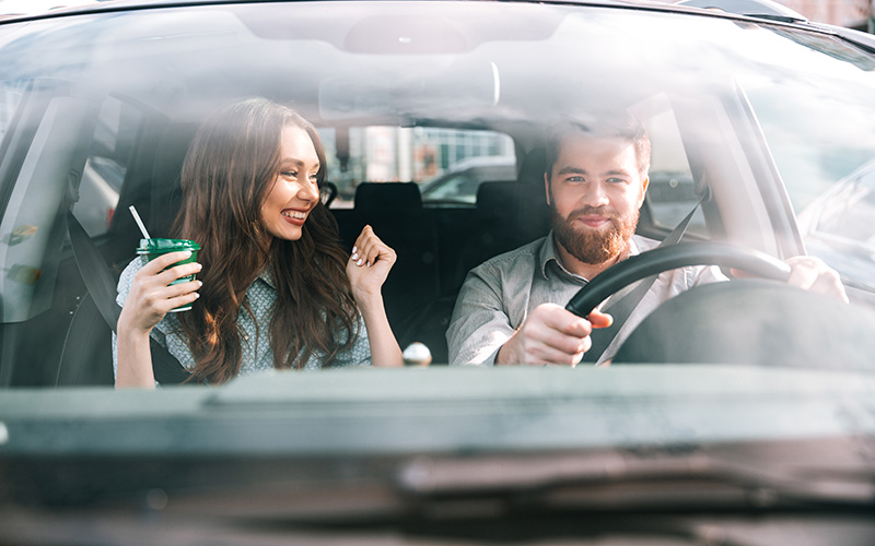 Mladi par uživa u vožnji nakon preuzimanja unajmljenog automobila na zračnoj luci Milan Bergamo, nasmiješeni u modernom vozilu dok napuštaju aerodromsko područje.