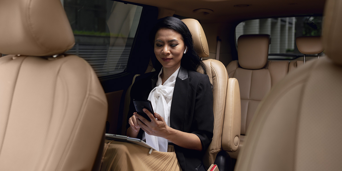 donna d’affari in van (interno), abitacolo confortevole di un noleggio auto 8 posti con passeggera che utilizza lo smartphone in un veicolo spazioso