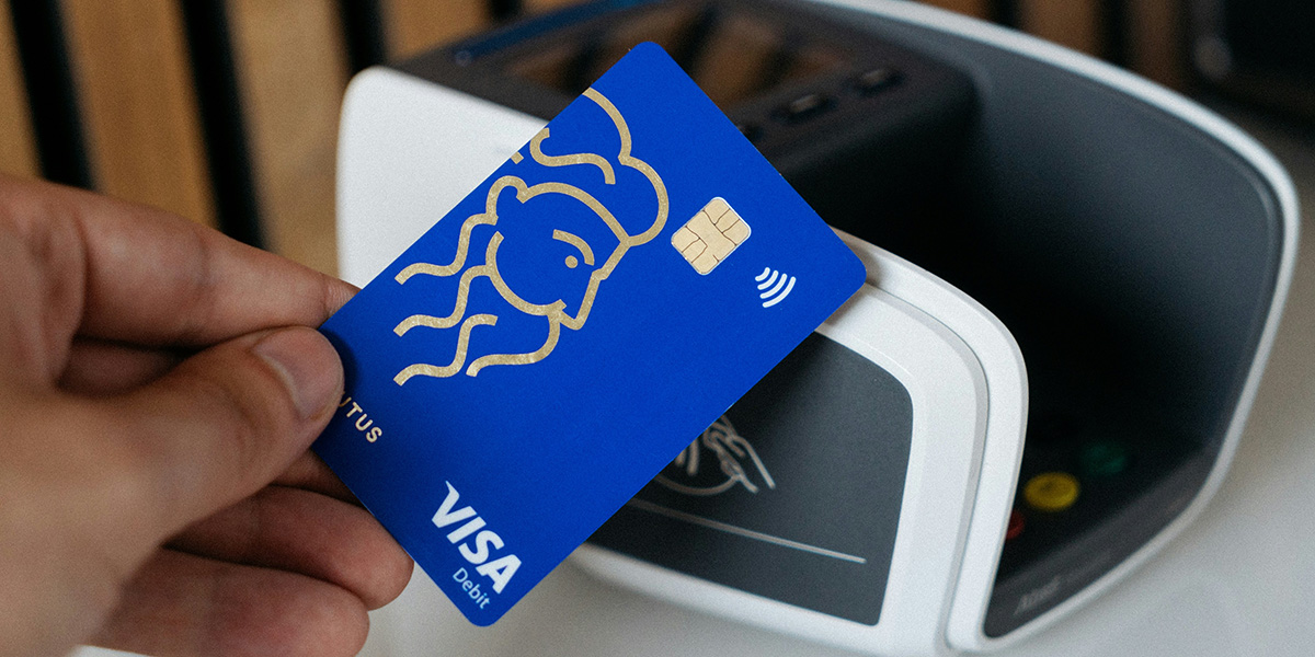 Primo piano di una carta di debito utilizzata per il pagamento su un terminale, che illustra come i viaggiatori possano completare il noleggio auto senza carta di credito utilizzando invece una carta di debito.