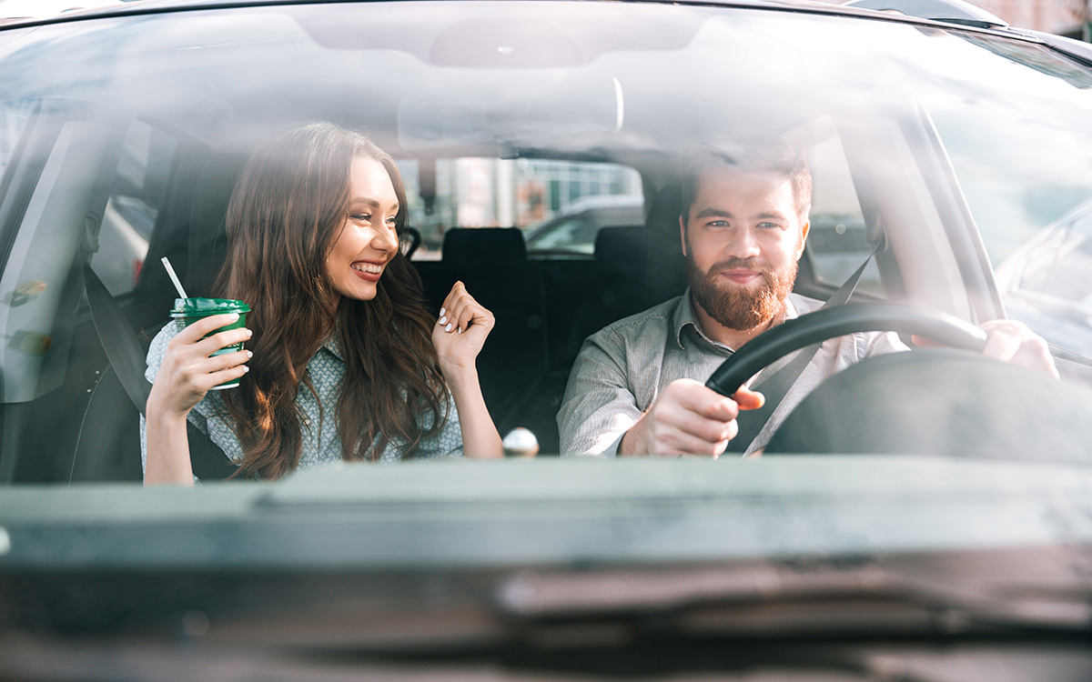 Modni portret para v avtomobilu, moški za volanom, pogled od spredaj, dekle z napitkom