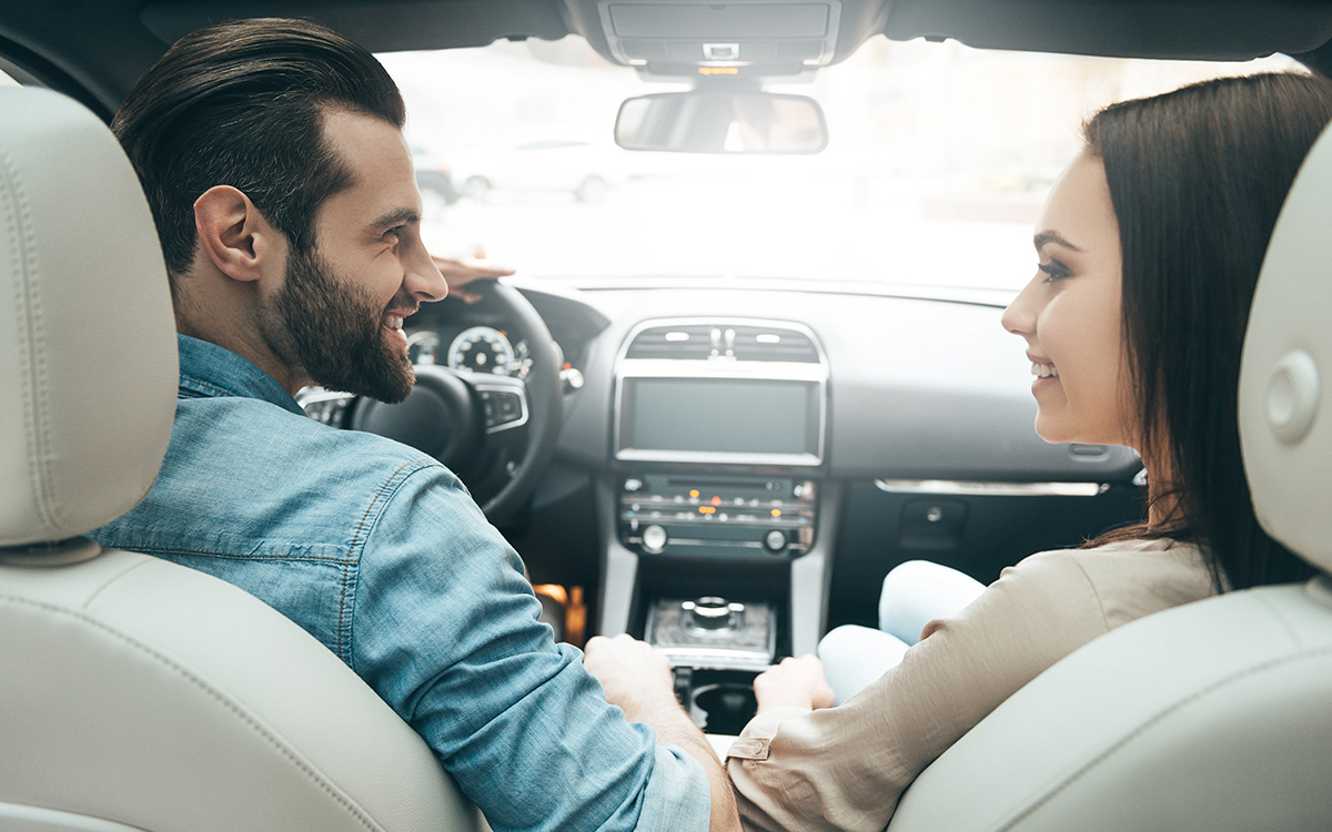 Coppia sorridente all’interno di un moderno abitacolo di un’auto a noleggio mentre inizia il viaggio dopo aver pagato il veicolo con una carta di debito invece che con una carta di credito.