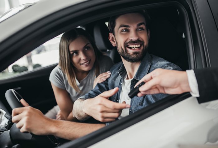 Un client reçoit les clés d’une voiture de location auprès d’un agent au moment du retrait après avoir réservé une location de voiture sans caution