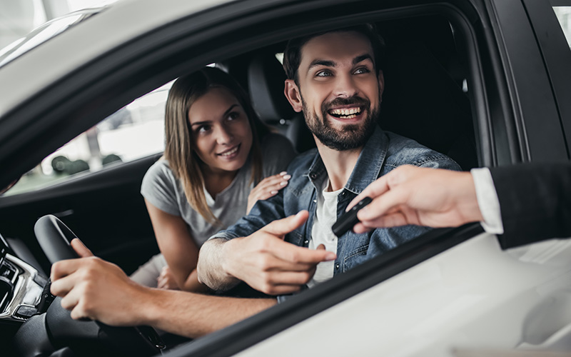 Cliente recibiendo las llaves del coche de un agente de alquiler en el momento de la recogida al reservar un alquiler coche sin fianza.