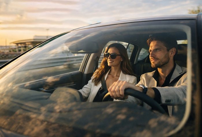 Un couple élégant conduisant une voiture de location au coucher du soleil, illustrant une situation de voyage typique après avoir réservé un véhicule de location avec des moyens de paiement alternatifs.