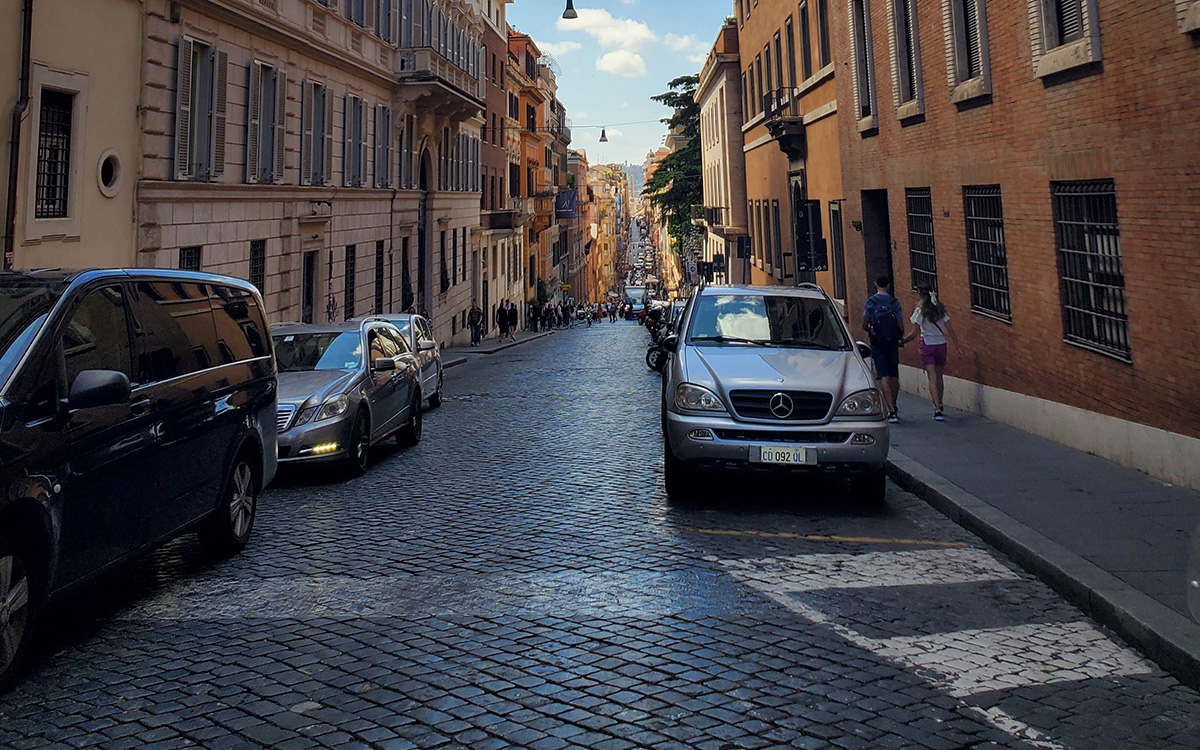 Cars parked along a picturesque cobblestone street during golden hour in Italy