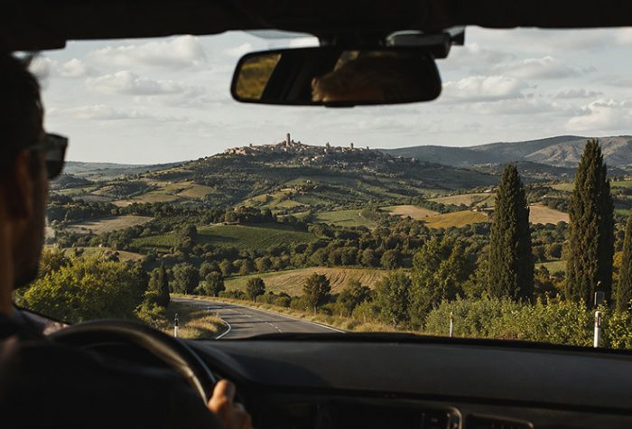 Driving in Italy along a scenic Tuscany road with beautiful hill views and sunshine inside the car.