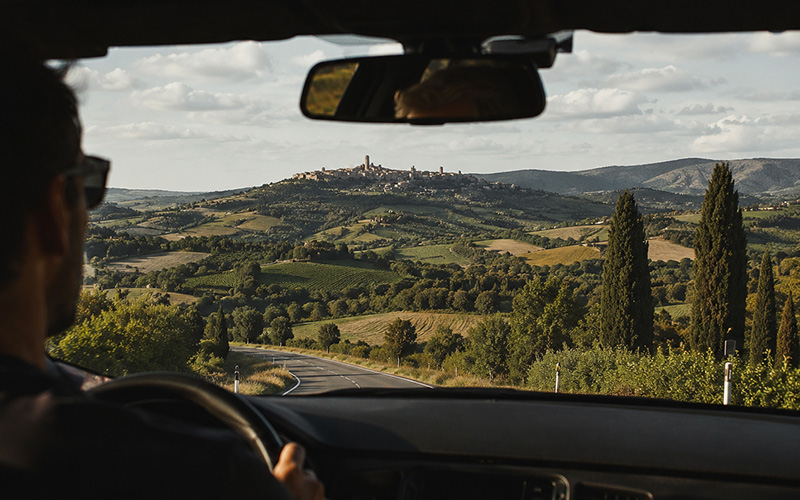 Driving in Italy along a scenic Tuscany road with beautiful hill views and sunshine inside the car.