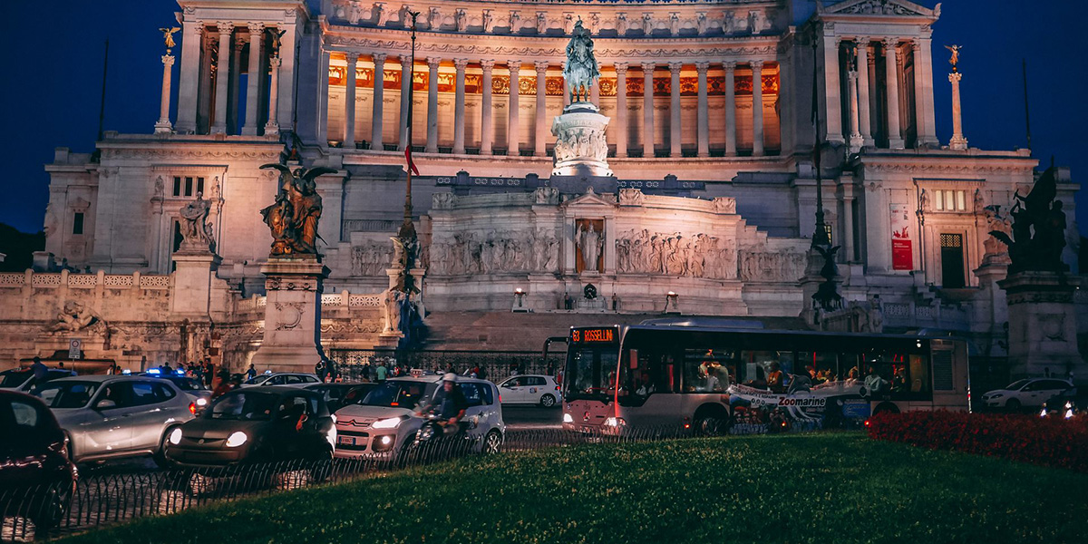Evening traffic in Rome passing the illuminated Altare della Patria monument in Piazza Venezia.