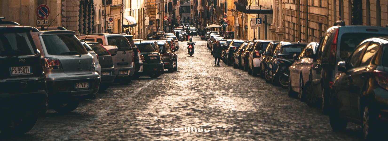 Historic Roman street filled with parked cars and traditional architecture near the city centre.