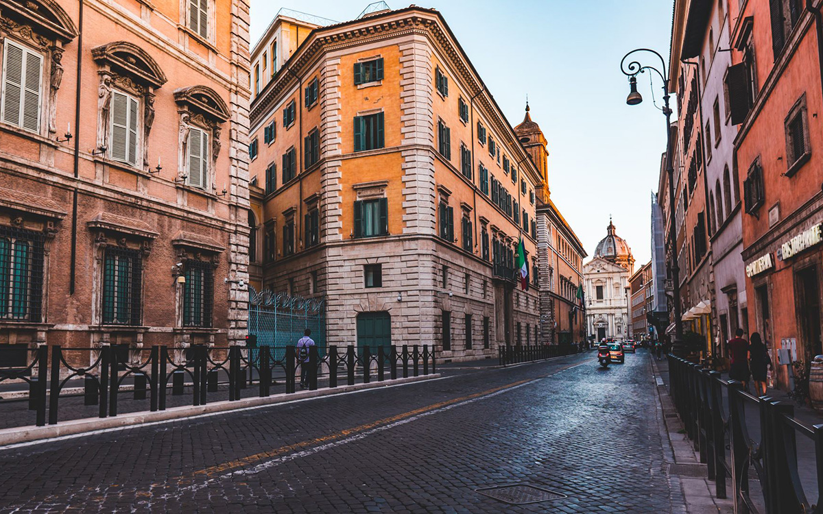 Historic street in central Rome with cars, scooters, and Renaissance buildings.