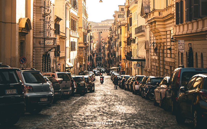 Parking in Rome on a narrow cobblestone street lined with parked cars in the historic city centre.