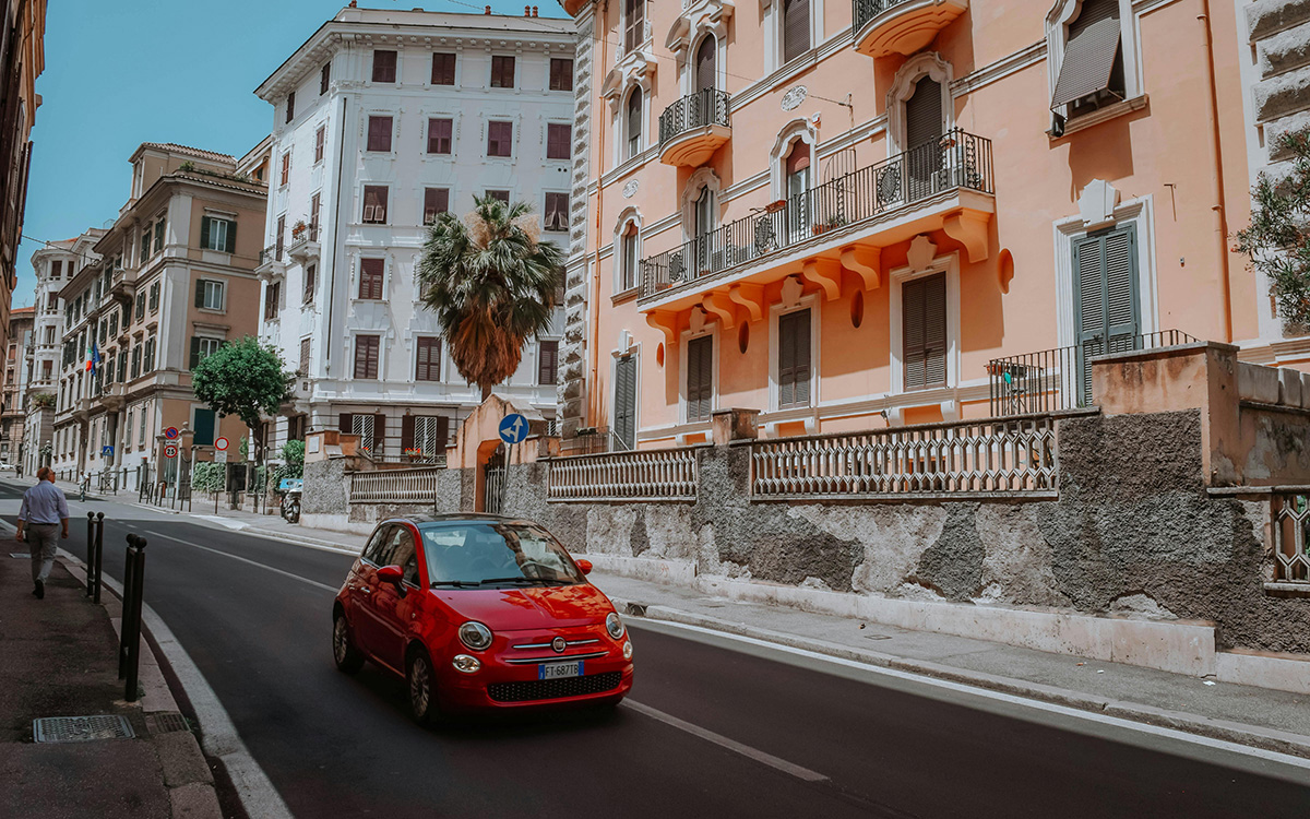 Small Fiat 500 red, driving through an Italian city street.