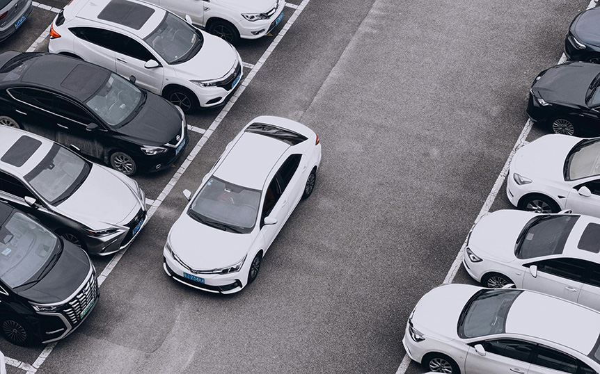 Aerial view of a rental car parking lot with a white car pulling out of the row