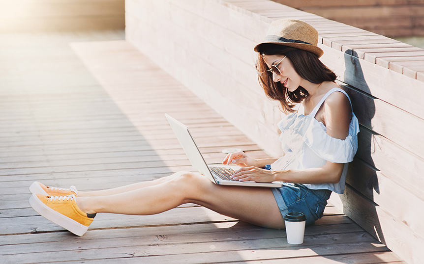 Traveler comparing car rental prices on a laptop while sitting on a sunny boardwalk